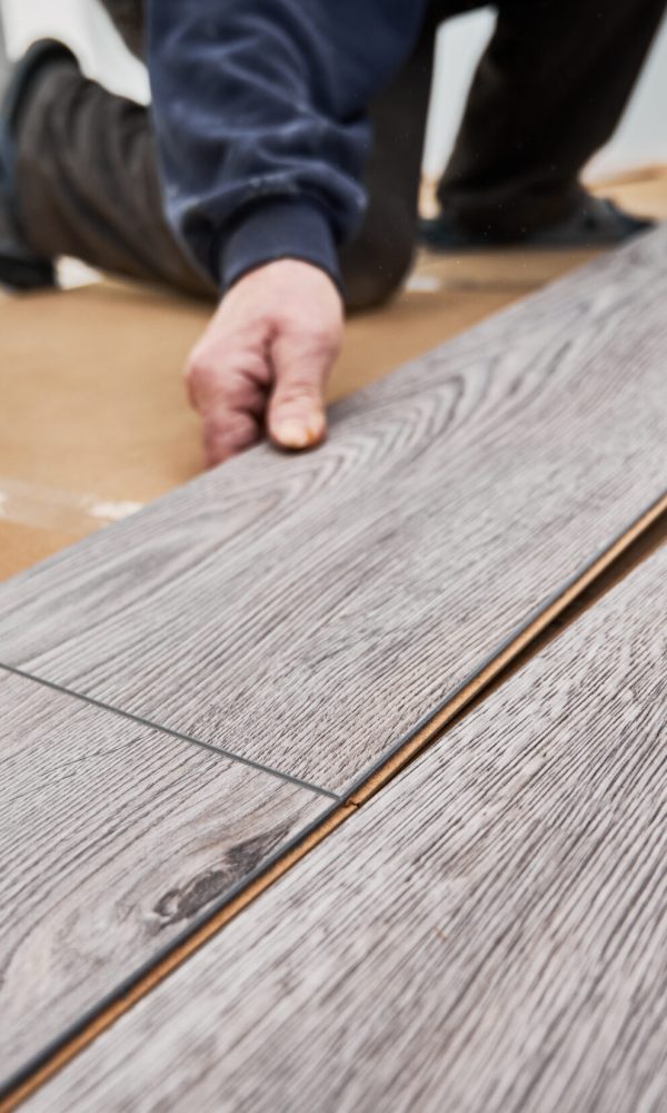 Close up of man construction worker installing laminate timber flooring in apartment under renovation. Male hands placing laminate planks on the floor at home. Flooring renovation concept.