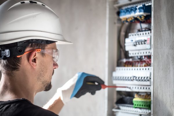 Man, an electrical technician working in a switchboard with fuses. Installation and connection of electrical equipment. Professional with tools in hand. concept of complex work, space for text. SSUCv3H4sIAAAAAAAEAI1Ry2rDMBC8F/oPRucYZMchdv+gh0LvoYe1tIlFFW3QoyWE/HslKyo6ld60M6vZnZ3b81PTsBmcEuyluaUq1krr4LwFr8hEmG8euEUj0dYISuXJKtA1OIMXi4EzRtAErRN8X0nmPPjg0KVhD0iAx1PUyOCvRN7okOumECsZf0SKvSNdNLJNxbgwJ+ZNOYFag0EKjhX+vvlD7NXIZDk5+b9gfnwU33BCI66rtcqyRY2QLR9yK/v89mjP9REgSEWV/y8SoFPDtlK6WCWUOVXfyC9rHuWboGC8TSuwYoNpogvMOoVxjJpY8AWci+2y4NUgEU9B52qOIb8aeKgyGTNLZbftu3EYdkPX7Uc+8h1nJWcSn0rWFnP0i4qUvVa4ShuwnostiGnfTv00tEOPuxYQx3bY81FwfpxG4PHw9x+hX0Y7sQIAAA==